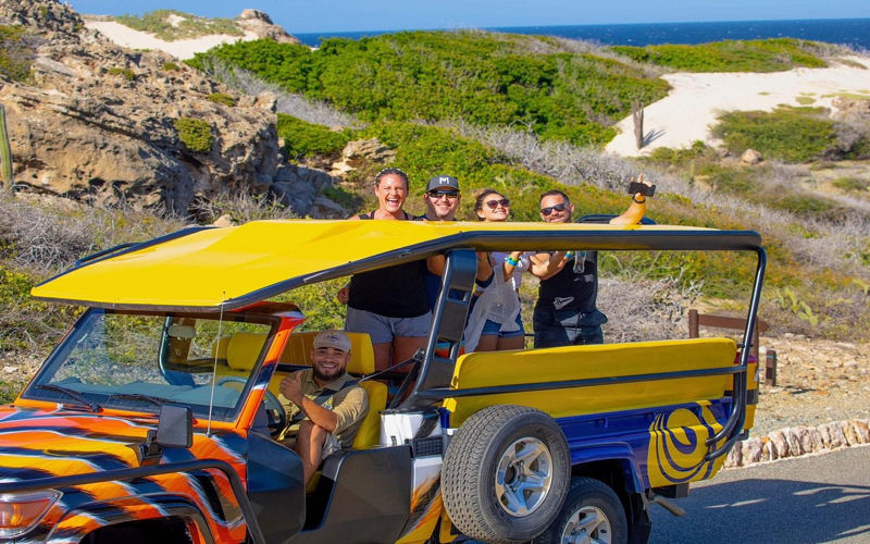 Happy group riding in a colorful open-air 4x4 jeep on an Aruba off-road adventure tour.