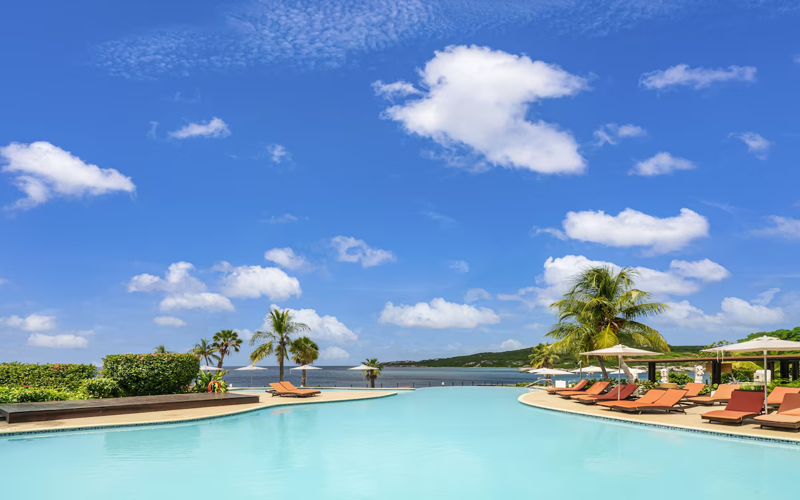 Expansive pool at Dreams Curaçao Resort with sun loungers and ocean backdrop.